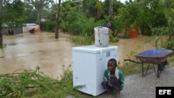 Un niño descansa junto a una lavadora después de las fuertes lluvias y vientos provocados por la tormenta tropical "Isaac" en Haití. 