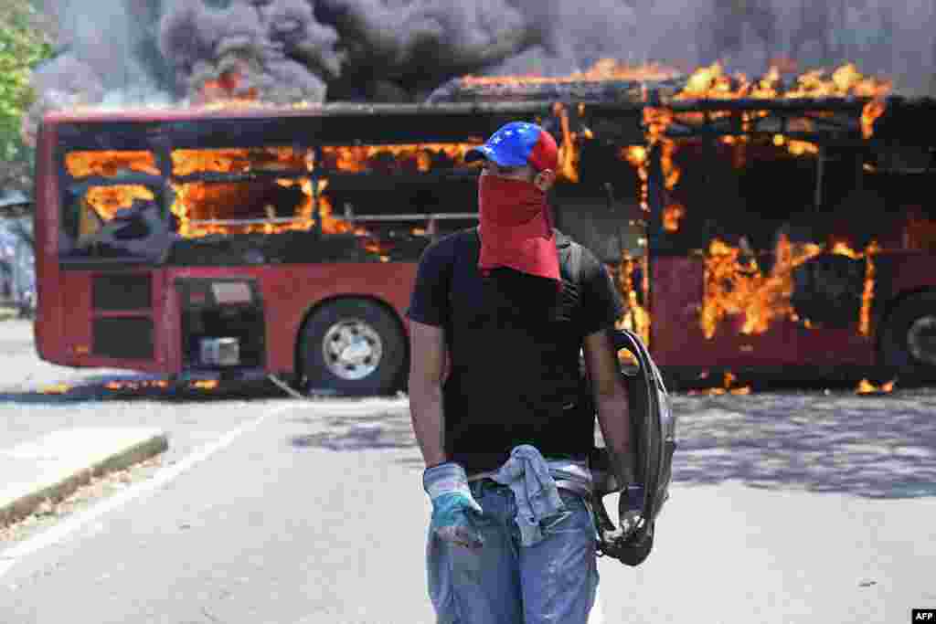 Un manifestante de la oposición camina cerca de un autobús en llamas durante los enfrentamientos con soldados leales a Nicolás Maduro. 
