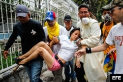 Un grupo de hombres carga a una mujer desmayada a causa de los gases lacrimógenos durante una confrontación de opositores con la Policía Nacional Bolivariana en Caracas.