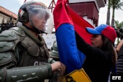 Una mujer sostiene una bandera de Venezuela frente a integrantes de la Guardia Nacional Bolivariana.