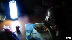 Niña come alumbrada por una lámpara de baterías durante un apagón en Cuba.