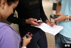 Tres jóvenes usan sus teléfonos móviles en La Habana.