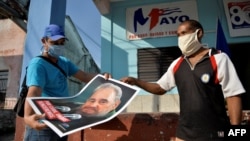 Dos cubanos muestran en San José de las Lajas, provincia de Mayabeque, un cartel con la imagen de Fidel Castro en vísperas de un 1ro de mayo que, según el gobierno, habrá que celebrar desde los hogares (Yamil Lage/AFP).