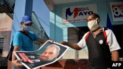 Dos cubanos decoran un muro con la imagen del fallecido dictador Fidel Castro, en vísperas del 1ro de mayo del 2020. (Yamil Lage/AFP/Archivo).