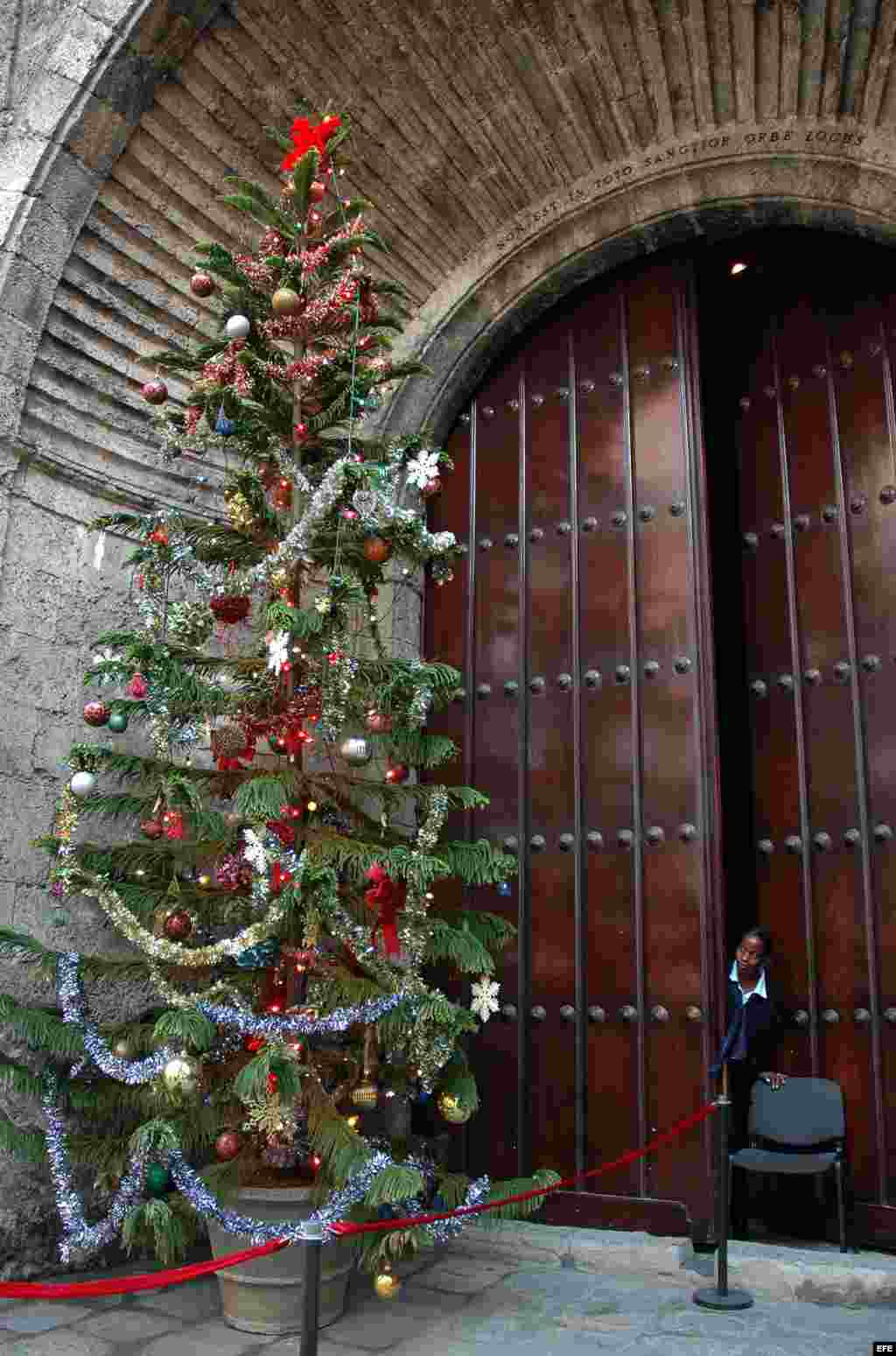 Una guardia de seguridad se asoma a observar un árbol de navidad colocado en la puerta de una sala de conciertos.