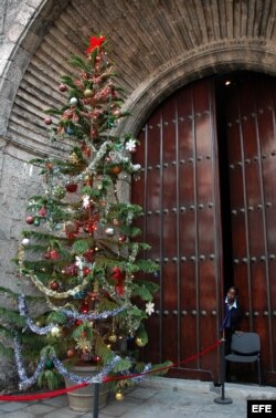 Una guardia de seguridad se asoma a observar un árbol de navidad colocado en la puerta de una sala de conciertos.