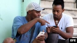 Dos personas navegan por internet desde un dispositivo móvil en una de las zonas habilitadas con Wi-Fi en La Habana.