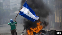 Un joven corre con la bandera de Nicaragua frente a unas llantas incendiadas ayer en la ciudad de Masaya (Nicaragua). EFE