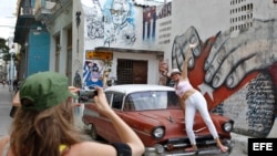 Una turista posa para fotos sobre un auto antiguo en La Habana.