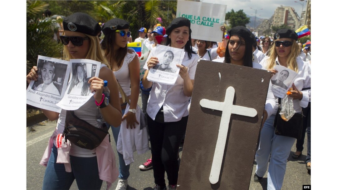 Un grupo mujeres sostiene fotografías de los rostros de las víctimas fatales de las protestas en Venezuela