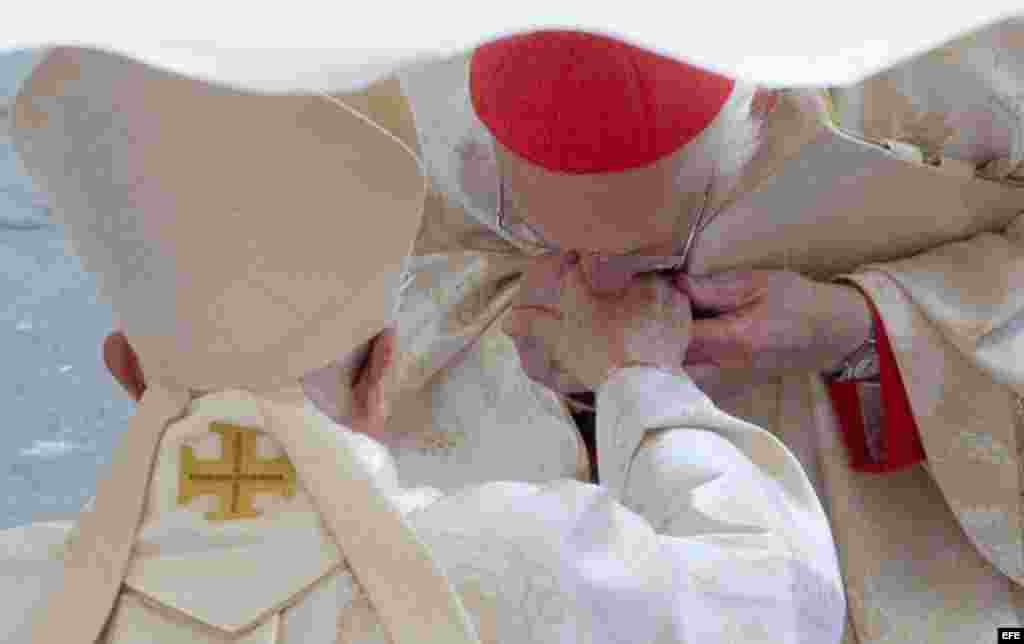 Un cardenal besa la mano del Papa emérito Benedicto XVI.
