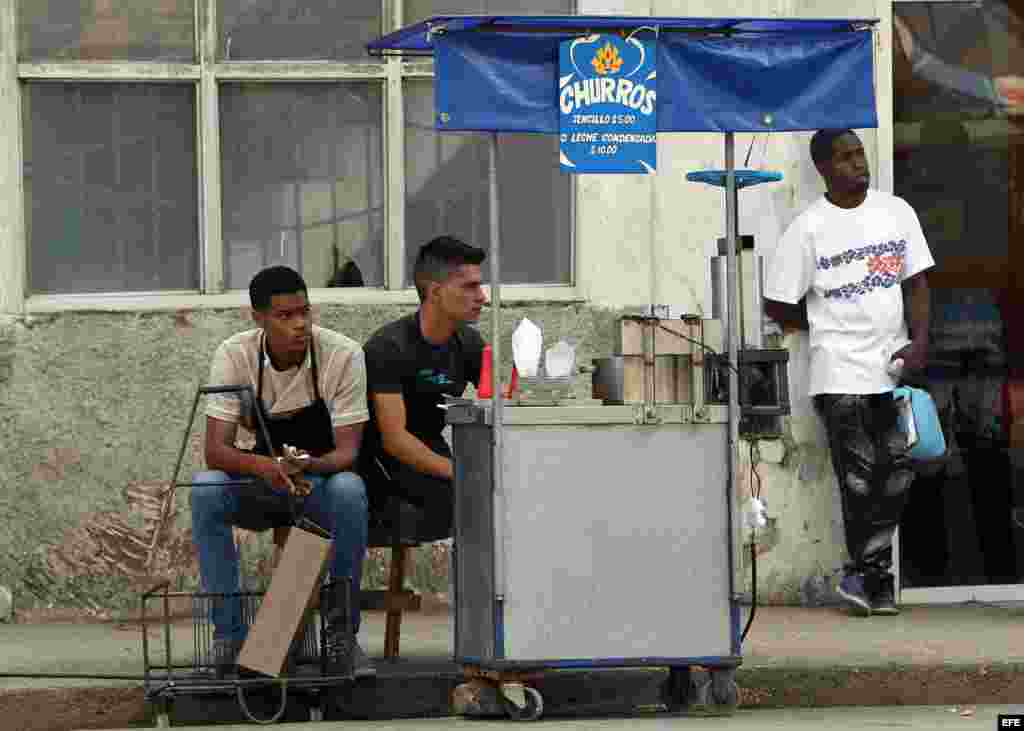 Dos jóvenes atienden un carrito de venta de churros.