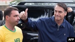 Jair Bolsonaro (d), junto a su hijo y candidato al senado, Flavio Bolsonaro, saluda al llegar a Villa Militar para votar en las elecciones generales de Brasil.