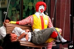 Fotografía de archivo del 27 de mayo de 1998 de un hombre chino durmiendo en las piernas de un maniquí de Ronald McDonald afuera de un restaurante McDonald’s en el sur de la plaza Tiananmen de Beijing. McDonald’s abrió su primera sucursal en China en 1990.
