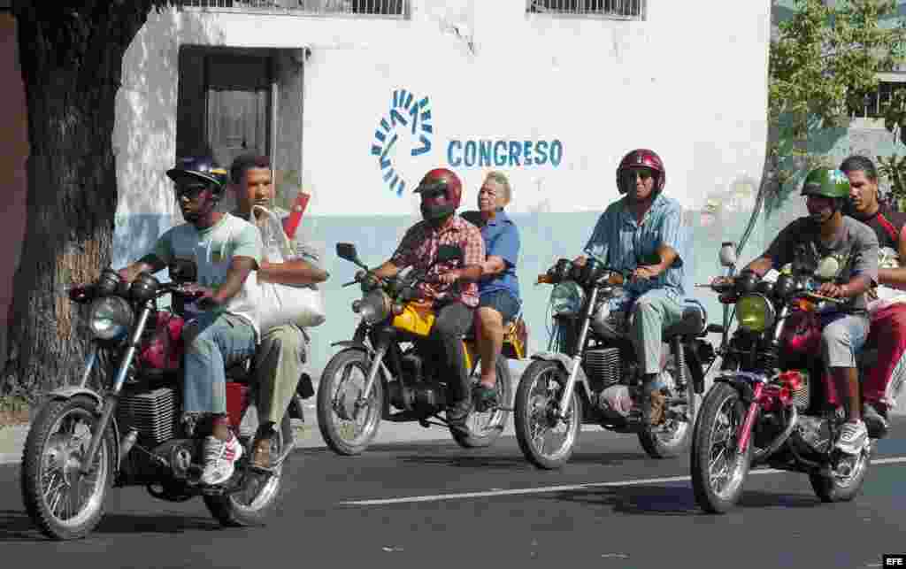 Several people traveling by motorbike taxi through the streets of Santiago de Cuba. 