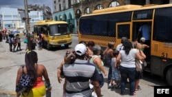 Varias personas hacen fila para subir a un ómnibus de una cooperativa de taxis colectivos en La Habana (Cuba). 