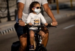 Una niña transportada en bicicleta usa un nasobuco para evitar el contagio del coronavirus, en La Habana.