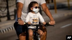 Una niña transportada en bicicleta usa un nasobuco para evitar el contagio del coronavirus, en La Habana, Cuba. AP Photo/Ramon Espinosa