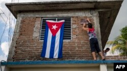 Una mujer adorna su casa con una bandera cubana / Foto: AFP