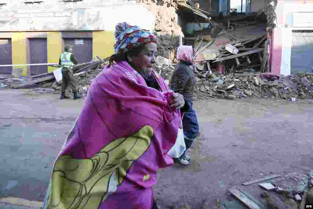 Mujeres caminan por una calle de Illapel junto a una casa destruida por el simo.