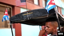 El conductor de un bicitaxi, adornado con banderas de Cuba y EEUU, espera la llegada de clientes en La Habana (Cuba).