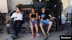 Un guardia se cubre la cara junto a migrantes de Cuba que descansan en un sofá dentro de un refugio en Nuevo Laredo.