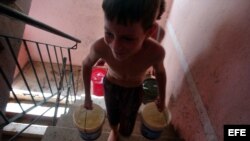 ARCHIVO. Un niño cubano carga dos cubos de agua por las escaleras de su casa.