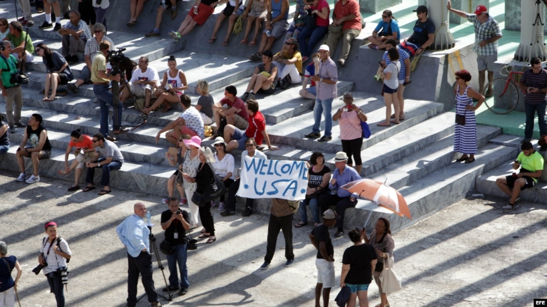 Un hombre muestra un cartel junto a decenas de curiosos y periodistas frente a la embajada de Estados Unidos en Cuba.