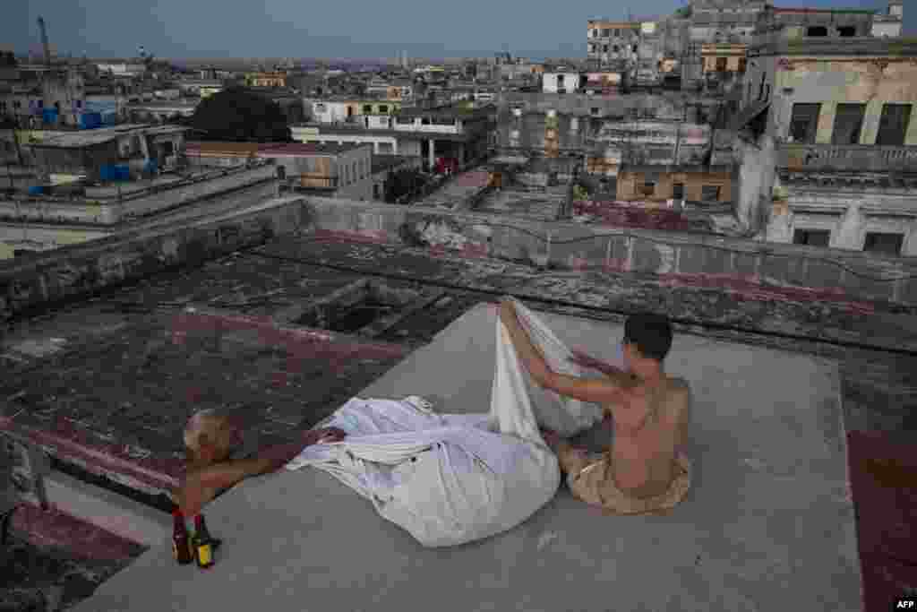 Alexis Mijan y su hijo, Bayron Miranda, doblan sábanas en la azotea de un edificio residencial al amanecer en La Habana Vieja, el 12 de agosto de 2026. YAMIL LAGE / AFP.