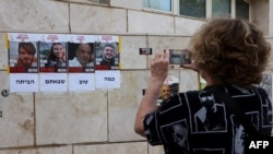 Una mujer toma una fotografía de carteles que dicen "En casa ahora" con el rostro de los cuatro rehenes.