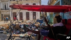 Un conductor de bicitaxi espera a los clientes junto a un montón de basura en La Habana, Cuba, el lunes 1 de junio de 2026. (Foto AP/Ramón Espinosa)