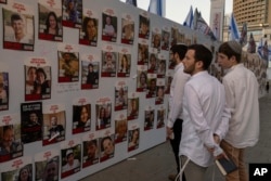 Jóvenes israelíes miran fotografías de israelíes desaparecidos y cautivos en Gaza, exhibidas en una pared en Tel Aviv, el viernes 20 de octubre de 2023. (Foto AP/Petros Giannakouris)