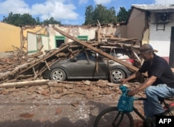 Un hombre pasa en bicicleta junto a una casa derrumbada y un automóvil sepultado bajo los escombros en la localidad de Chitré, a unos 250 km al suroeste de la ciudad de Panamá, el 10 de octubre de 2026.