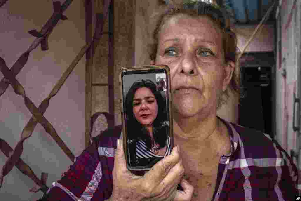 Yanelis Leon habla por videollamada desde Estados Unidos durante una entrevista mientras su madre, Natacha González, quien cuida de sus dos hijos, sostiene el celular en la entrada de su casa en Cienfuegos. &nbsp;(AP Foto/Ramón Espinosa)