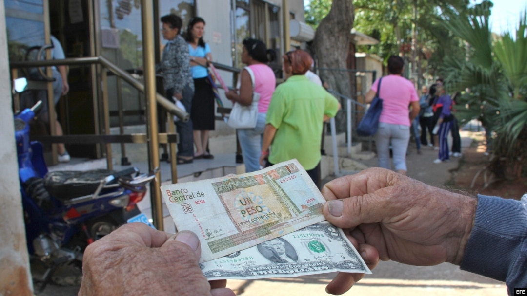 Un hombre muestra un peso convertible cubano y un dólar estadounidense frente a una oficina de la Western Union en La Habana.