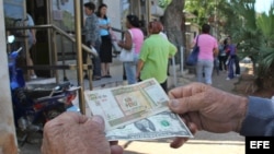 Un hombre muestra un peso convertible cubano y un dólar estadounidense frente a una oficina de la Western Union en La Habana.