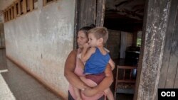 Una madre carga en brazos a su pequeño hijo frente a una de las aulas convertidas en vivienda. (Foto: Dan Gabriel)