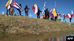 Migrantes que buscan asilo en Estados Unidos ondean banderas durante una misa binacional para recordar a los migrantes que han muerto intentando llegar a ese país en las orillas del Río Grande en Ciudad Juárez, México. (Herika Martínez/AFP)