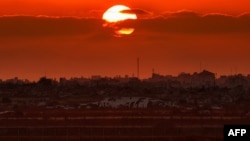 Esta imagen, tomada desde una posición en la frontera israelí con la Franja de Gaza, muestra el sol poniéndose tras edificios en el territorio palestino el 10 de junio de 2026. (Foto de Jack GUEZ / AFP)
