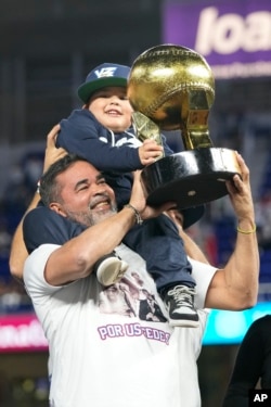 El técnico venezolano Ozzie Guillén y su nieto sostienen el trofeo después de la victoria del equipo por 3-0 sobre República Dominicana en el partido de campeonato de la Serie del Caribe de béisbol, el 9 de febrero de 2024, en Miami. (Foto AP/Wilfredo Lee)