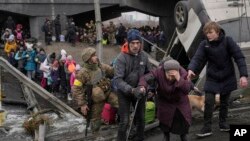 Una anciana recibe ayuda mientras cruza el río Irvin, bajo un puente destruido por un ataque aéreo ruso, mientras civiles huyen de la localidad. (AP/Vadim Ghirda).
