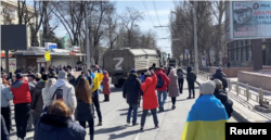 Los manifestantes, algunos con banderas ucranianas, cantan "vete a casa" mientras los vehículos militares rusos invierten el rumbo en la carretera, en una manifestación pro-Ucrania en medio de la invasión de Rusia, en Jersón, el 20 de marzo de 2022