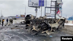 La gente pasa junto a un vehículo destruido en una carretera, en medio de la invasión rusa de Ucrania, en Bucha, Ucrania, el 2 de marzo de 2022 en esta imagen fija tomada de un video.