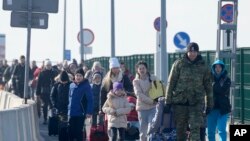 Un guardia fronterizo polaco (derecha) ayuda a los refugiados ucranianos a llegar a Polonia en el cruce fronterizo de Korczowa, Polonia, el sábado 26 de febrero de 2022. (AP Foto/Czarek Sokolowski)