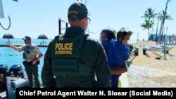 Agente de la Patrulla Fronteriza conversa con una migrante cubana que carga a un niño en brazos