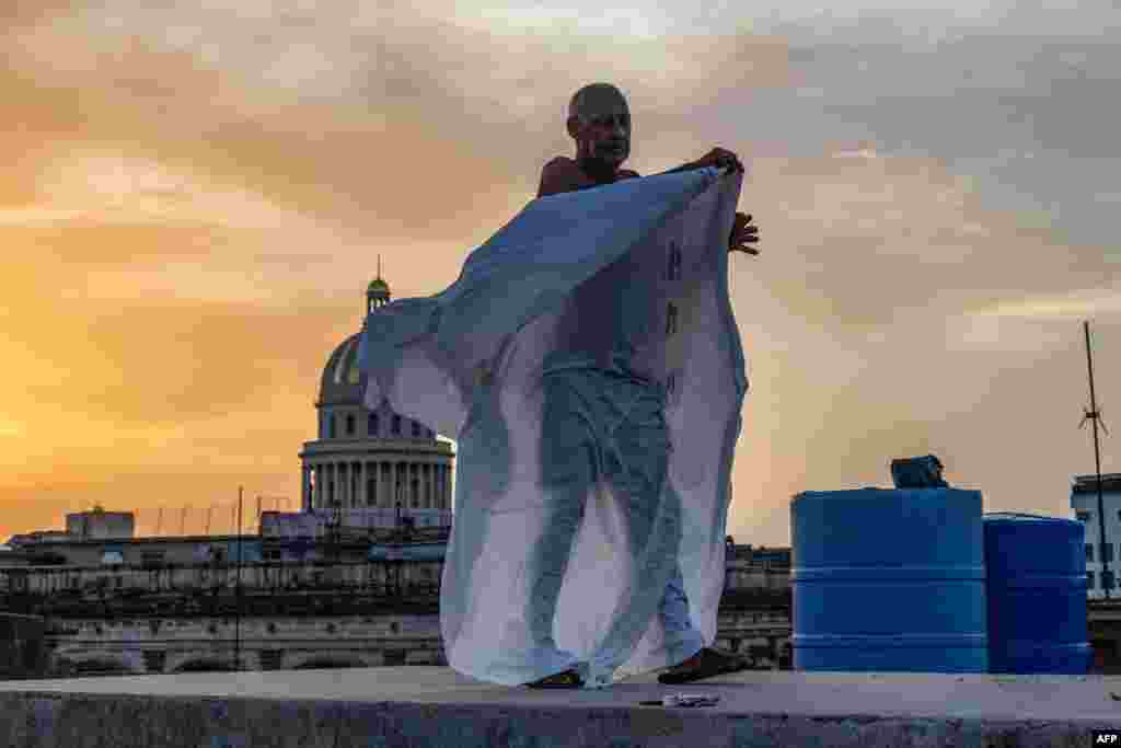 Alexis Mijan acomoda las sábanas de una cama improvisada en la azotea de un edificio residencial al atardecer en La Habana Vieja, el 12 de agosto de 2026. YAMIL LAGE / AFP.