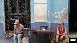  Un hombre repara zapatos, mientras otro vende una vieja máquina de coser en La Habana.