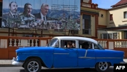 Un "almendrón" pasa junto a un cartel que muestra al fallecido dictador cubano Fidel Castro, su hermano Raúl Castro y el gobernante Miguel Díaz-Canel.