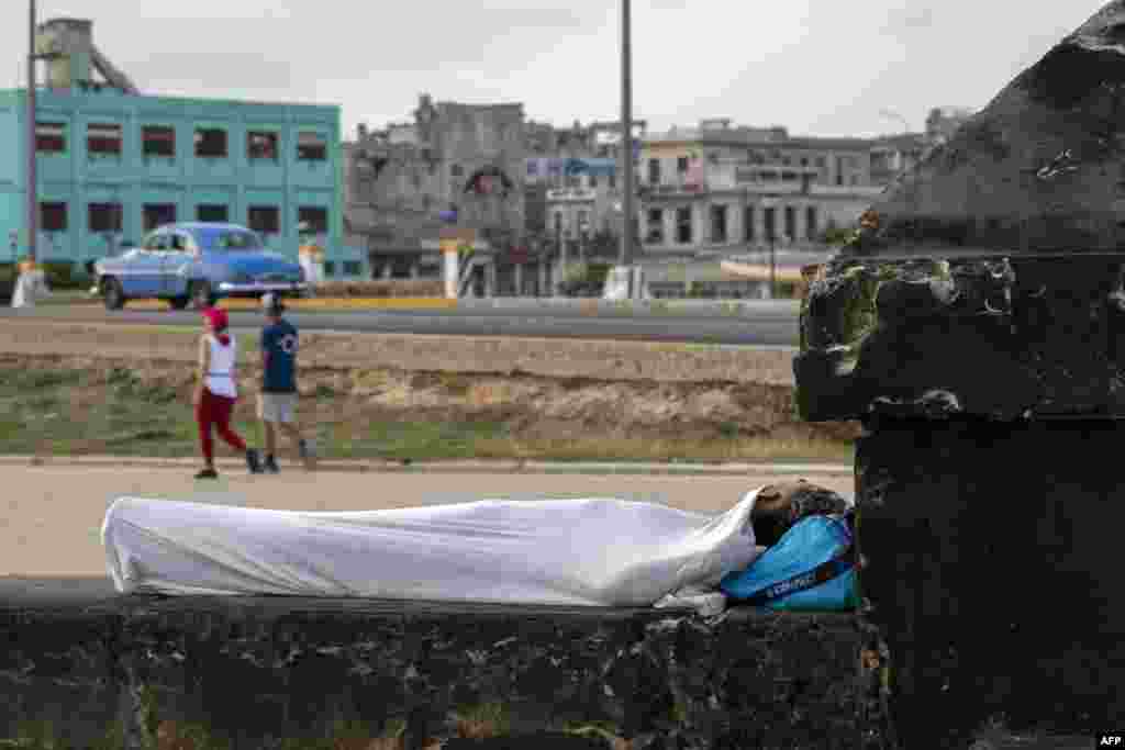 Una persona duerme envuelta en una sábana sobre el muro del Malecón al amanecer en La Habana, el 13 de agosto de 2026.  YAMIL LAGE / AFP.