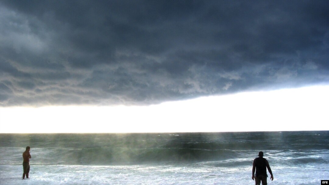Dos hombres observan las fuertes olas y el cielo nublado en una playa del oeste de La Habana. Archivo.